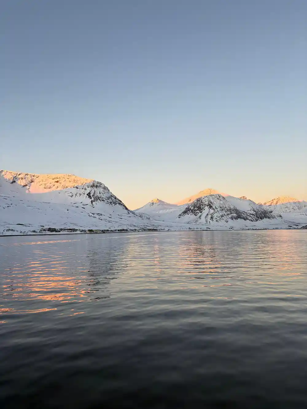 Golden-lit mountains reflecting in still fjord water
