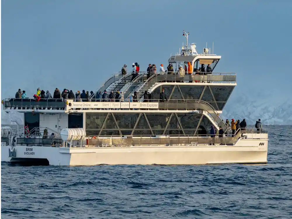 Large passenger boat with people on deck and snowy peaks
