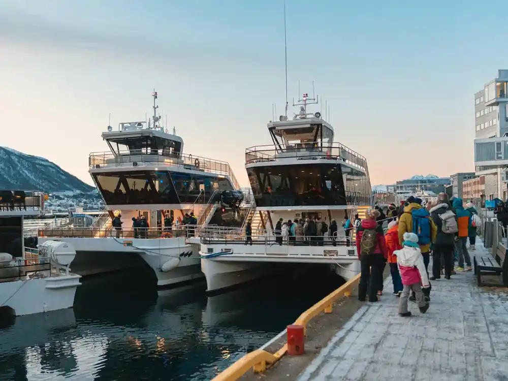 Multiple boats docked at waterfront with mountains and buildings
