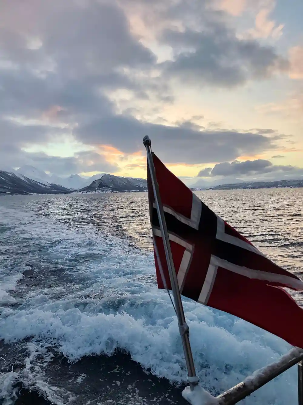 Norwegian flag on boat bow with snowy mountains behind