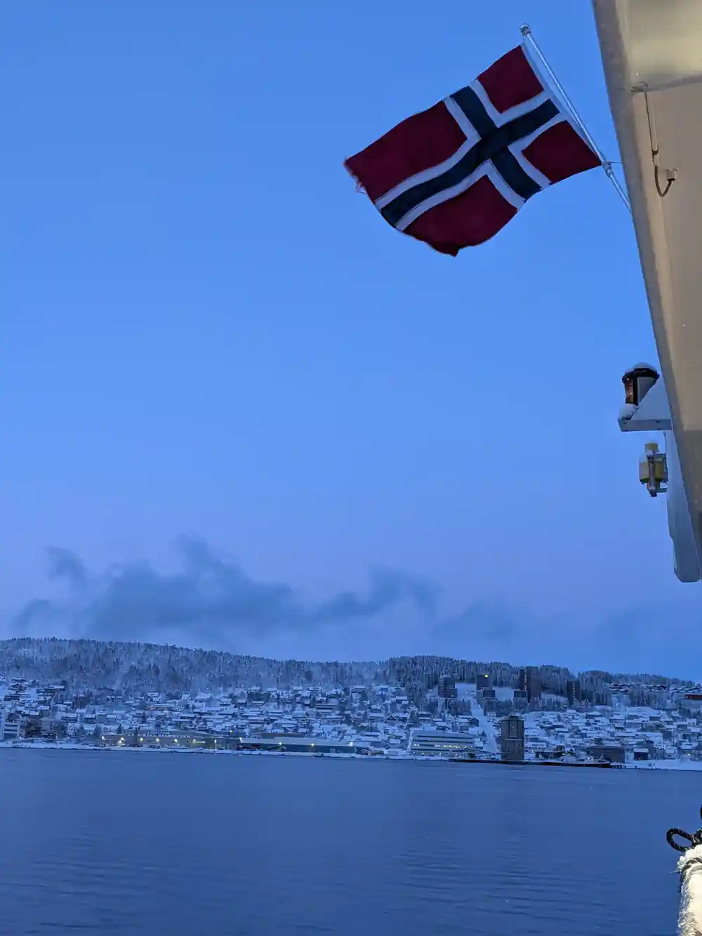 Norwegian flag flying from ferry with snowy coastal town