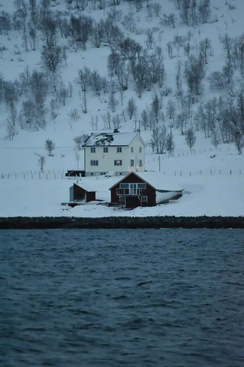 Red and white house on snowy hillside by water
