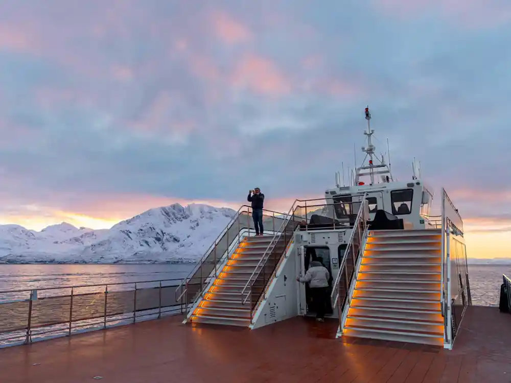 Ship with illuminated ramps at dock with snowy mountains