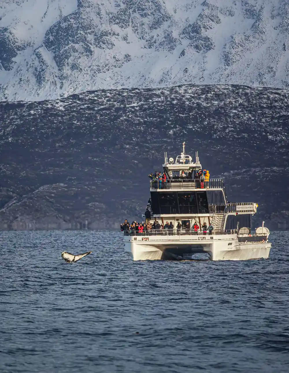 Small boat with passengers near snow-covered mountain slope