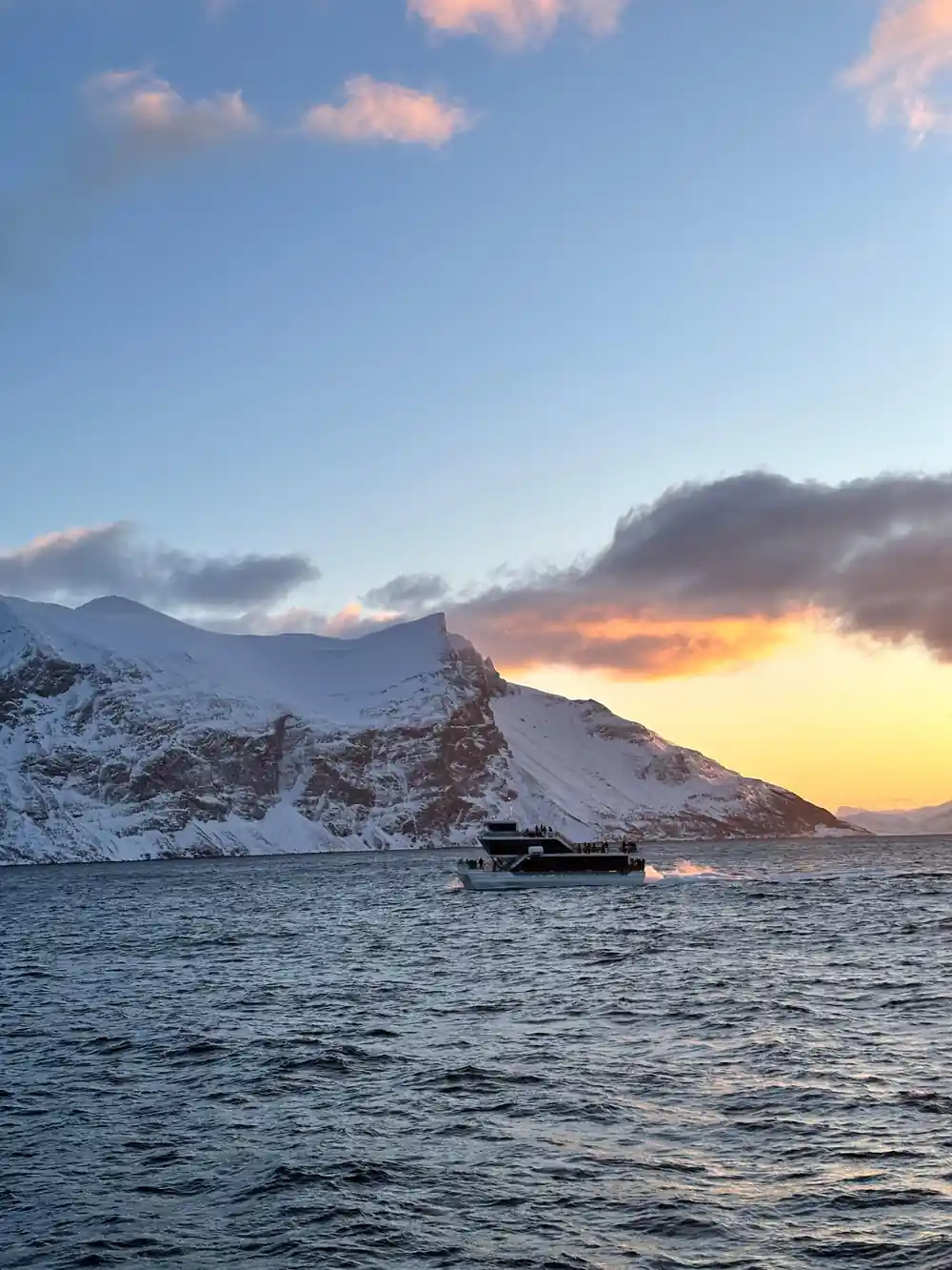 Small fishing boat in bay with snowy mountain at sunset