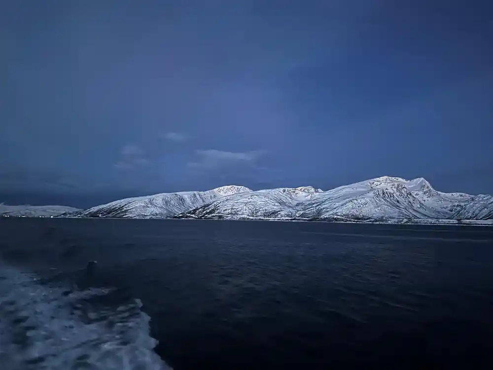 Snow-covered mountain range across frozen blue water