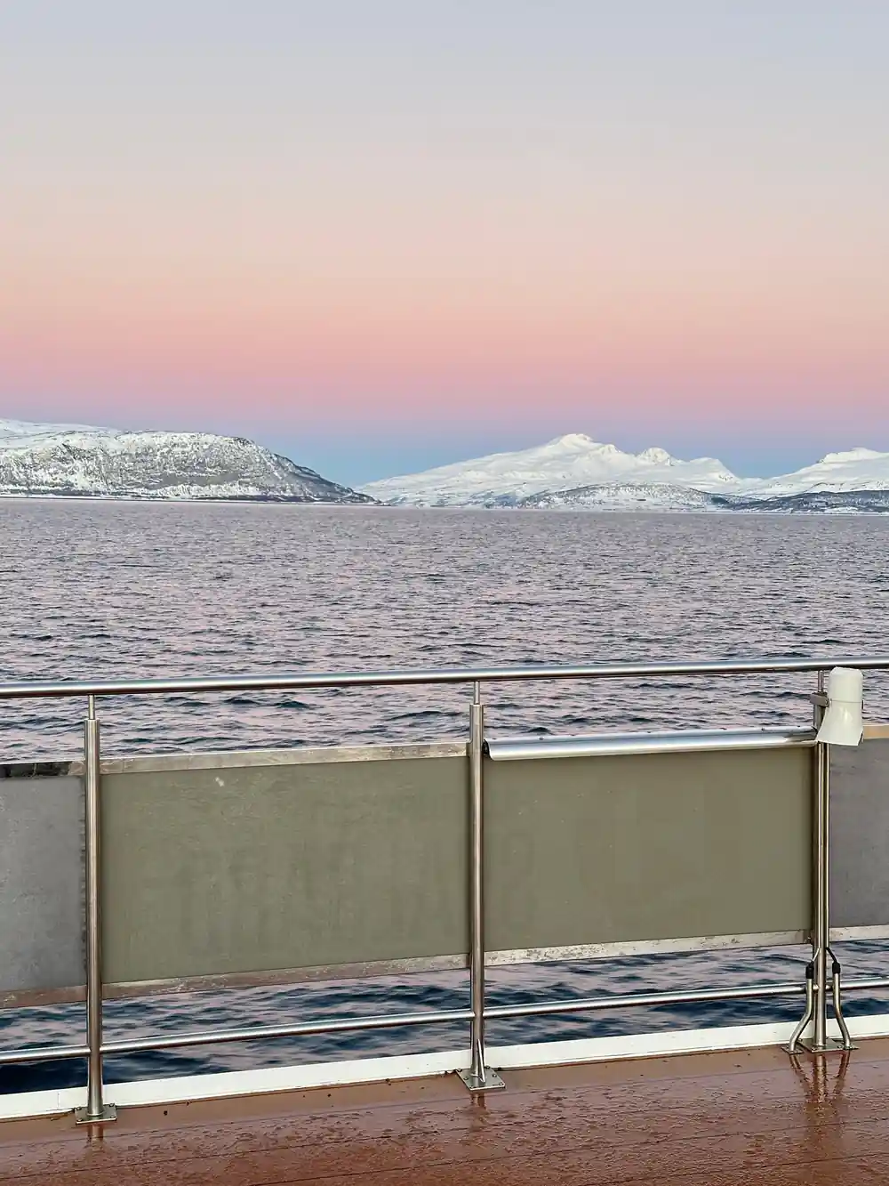 Snow-covered mountains across water from boat deck railing