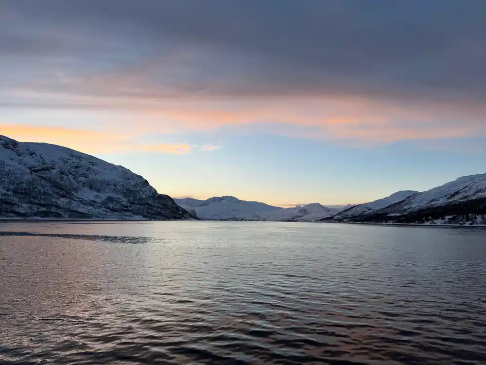 Snow-covered mountains across water at dusk with pink sky