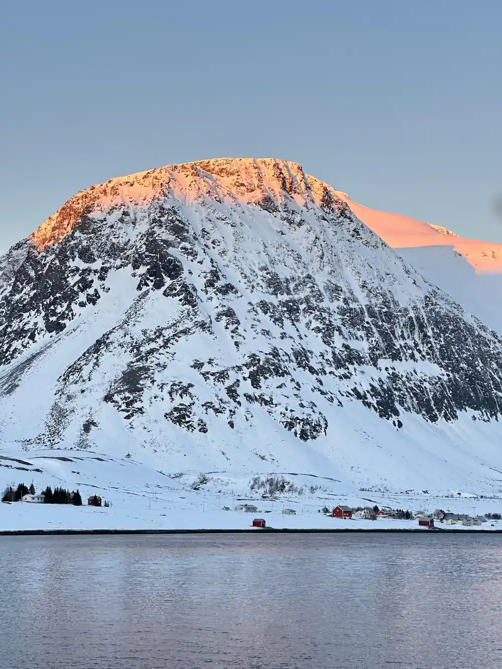 Steep snow and rock mountain peak lit by morning sun