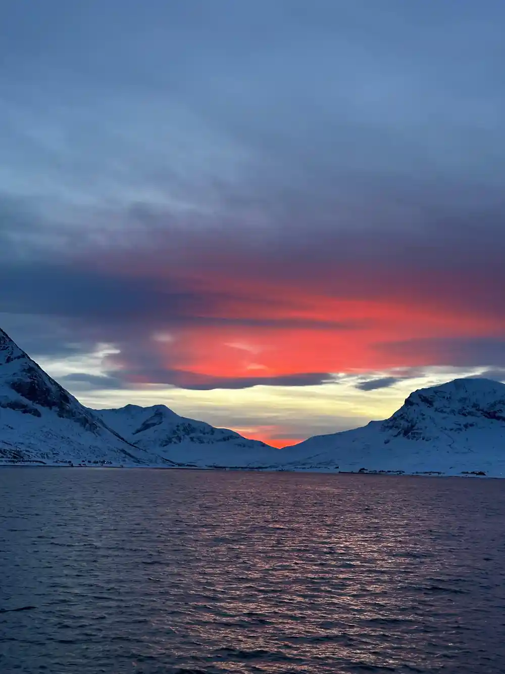 Sunset over snowy mountains and dark water fjord