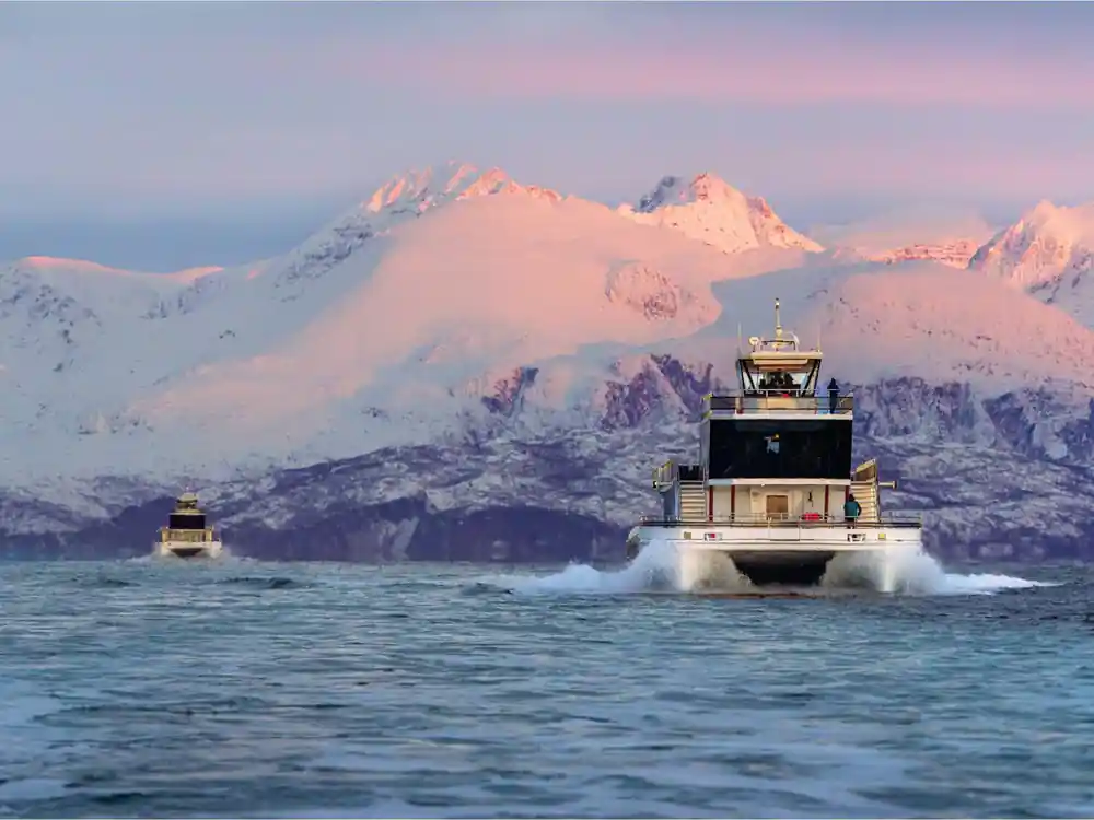 Two boats moving through water with pink-lit snowy mountain